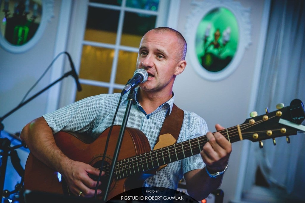 Paweł śpiewa i gra na gitarze akustycznej.